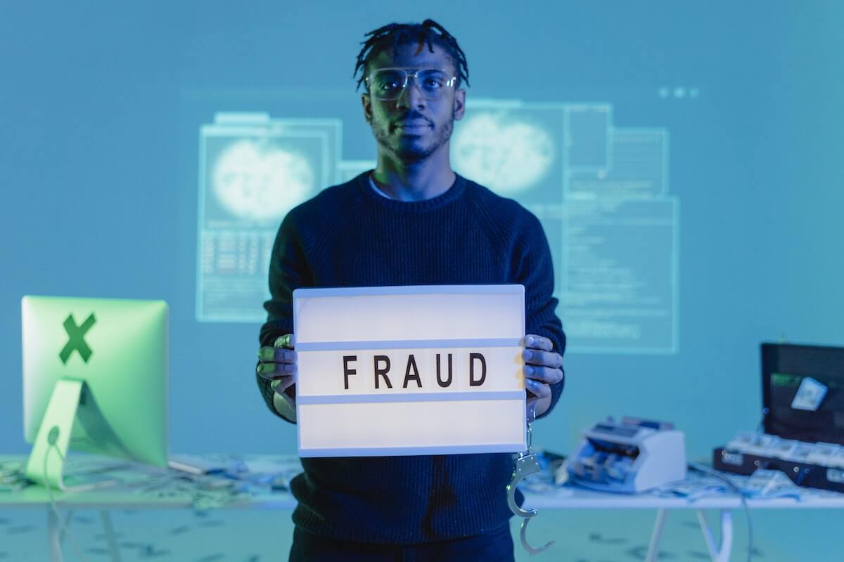 man holding fraud sign in front of computer and cash