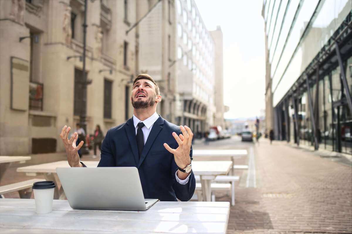 man in suit cursing at sky while on laptop outside in public
