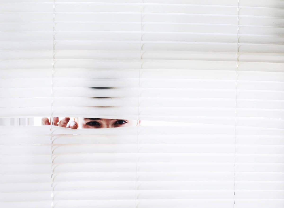 a man keeping a suspicious, watchful eye through blinds